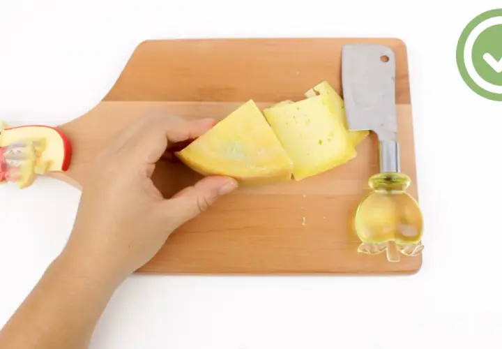 Mano che tiene un pezzo di formaggio giallo su un tagliere di legno, pronto per imparare come tagliare il formaggio a spicchi con un coltello.