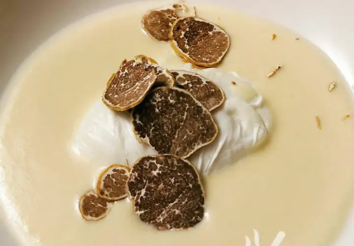 Uovo pochè su una cremosa fonduta, guarnito con scaglie di tartufo nero. Un piatto raffinato e profumato.