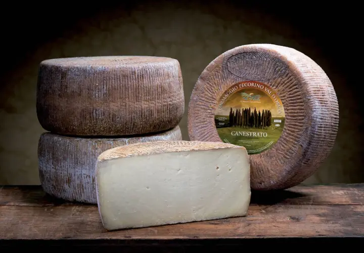 Formaggi di pecorino stagionato, uno intero con etichetta e uno tagliato a cuneo, su un tavolo di legno scuro.