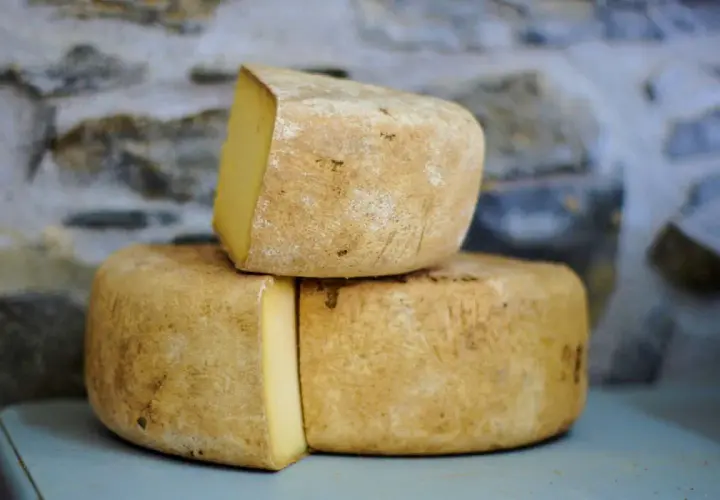 Formaggio di fossa stagionato, con crosta rustica e pasta gialla, impilato su uno sfondo di pietra grezza.
