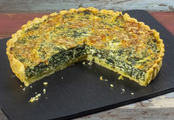 Una fetta di torta salata ricotta e spinaci, con crosta dorata e ripieno cremoso, servita su una lavagna scura.