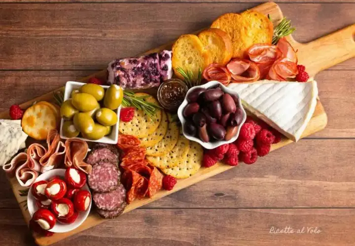 Un invitante tagliere salumi e formaggi con olive, lamponi, pane tostato e vari salumi.
