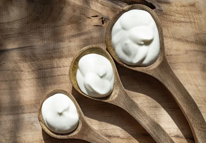 Tre cucchiai di legno pieni di panna da cucina, su un tagliere rustico.