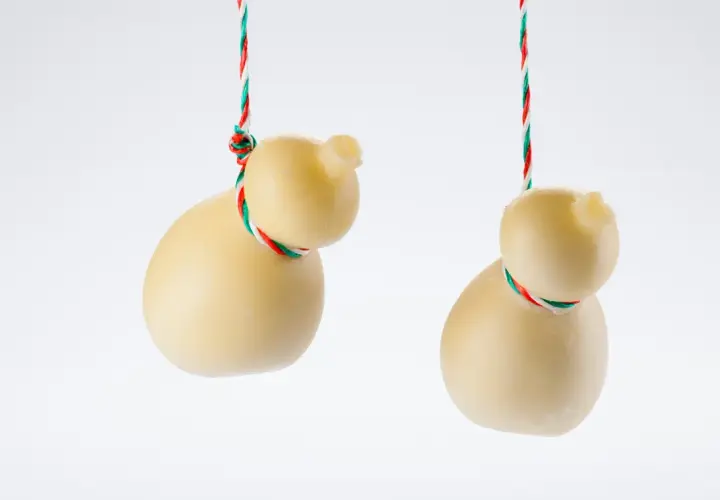 Due scamorze appese, una con la sua forma a pera, l'altra più tondeggiante. Entrambe sono legate con un filo tricolore. Ricorda che la scamorza contiene lattosio.
