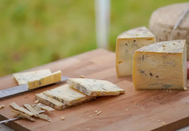 Formaggio stagionato con venature di muffa blu e verde su un tagliere di legno. Alcune fette sono già state tagliate.
