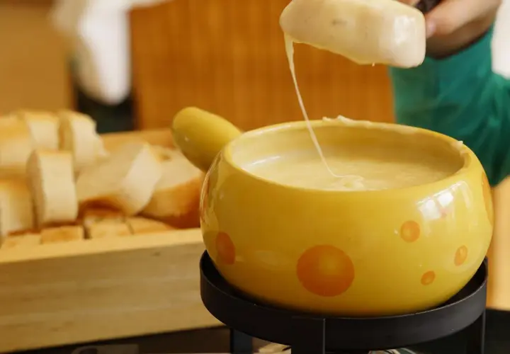 Un pezzo di pane viene intinto in una fonduta di formaggio filante, un modo delizioso per fondere il formaggio.