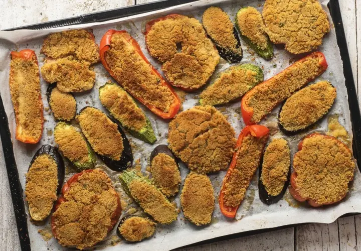 Verdure gratinate al forno con formaggio, un tripudio di sapori e colori su una teglia. Melanzane, zucchine e peperoni ripieni di pangrattato croccante.