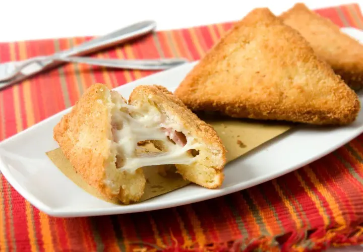 Mozzarella in carrozza dorata e filante, preparata in friggitrice ad aria, servita su un piatto bianco con tovaglietta a righe rosse.
