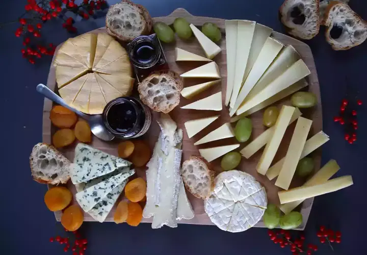 Un tagliere ricco di formaggi francesi, con pane, uva, albicocche secche e marmellata.