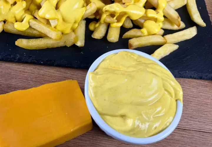 Patatine fritte ricoperte di cremosa salsa cheddar, con un blocco di formaggio e una ciotola di salsa a lato.