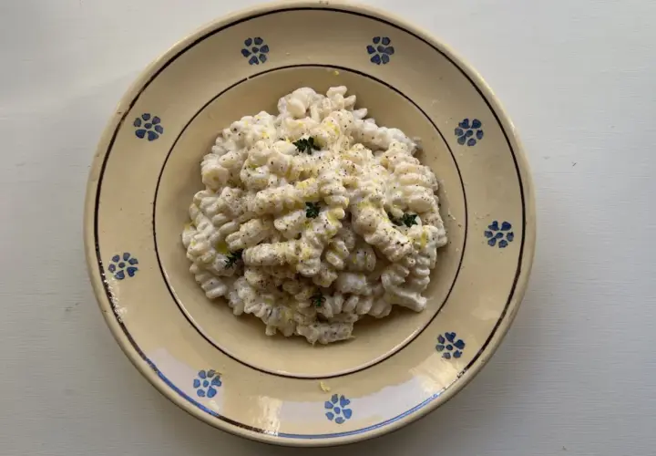 Piatto di pasta ricotta e limone, condita con erbe aromatiche e pepe nero, servita in un piatto di ceramica decorato.