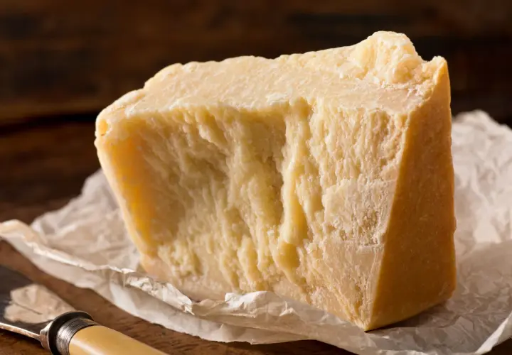 Un pezzo di formaggio stagionato, ideale per chi cerca un formaggio senza lattosio, su carta da forno con un coltello.