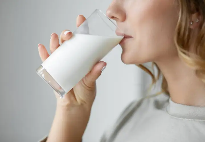 Donna bionda beve un bicchiere di latte. C'è chi dice che il latte fa ingrassare, ma lei sembra goderselo.