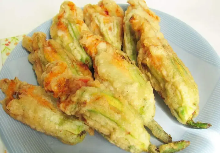 Fiori di zucca ripieni di ricotta, dorati e croccanti, serviti su un piatto azzurro.