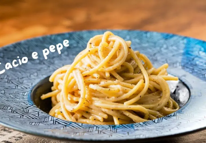 Un piatto di spaghetti fumanti, conditi con una cremosa salsa cacio e pepe, serviti in un piatto blu decorato.
