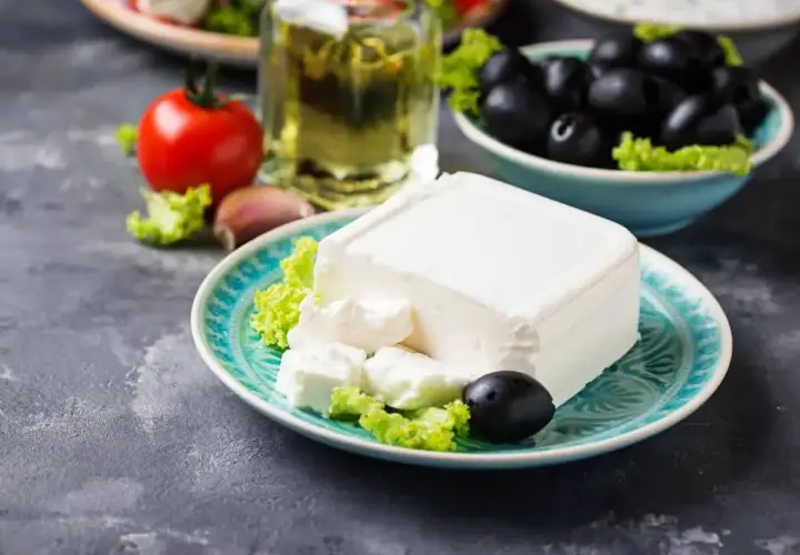 Un blocco di feta su un piatto turchese, con olive, pomodoro e olio d'oliva. La feta proprietà è l'ingrediente principale di questa deliziosa insalata greca.