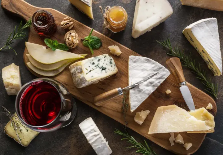 Tagliere con vari formaggi, tra cui un formaggio inglese, pere, noci, miele e vino rosso.