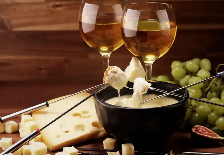 Fonduta di formaggio con pane e uva, accompagnata da vino bianco. Un'ottima fonduta di formaggio con cosa si accompagna? Con questi ingredienti, è perfetta!