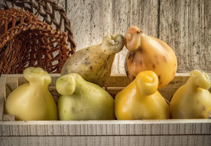 Formaggi a pera, tra cui una caciotta affumicata, in una cassetta di legno e un cestino intrecciato.