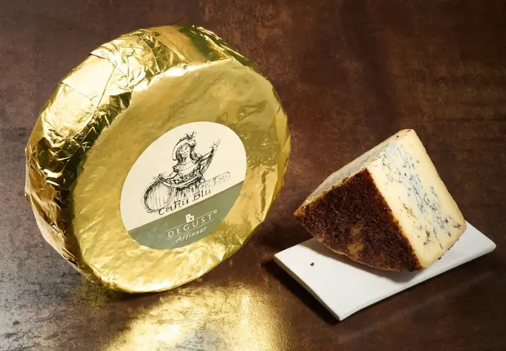 Formaggio blu con crosta scura, accanto a una forma intera avvolta in carta dorata. Questo cacio cos'è? Un'eccellenza da gustare.