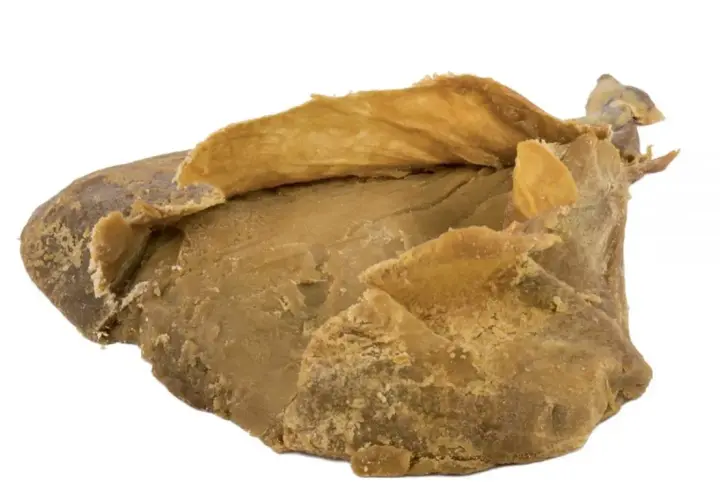 Blocco di caglio animale essiccato, di colore giallo-marrone, con una consistenza irregolare e sfogliata.