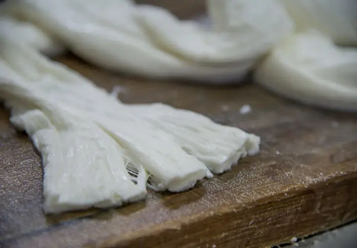Formaggio a pasta filata, lavorato a mano, con fili bianchi e morbidi su un tagliere di legno.