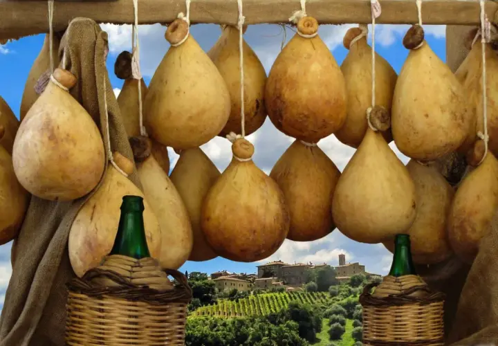 Formaggio cacio appeso, con sfondo di un borgo toscano e vigneti.