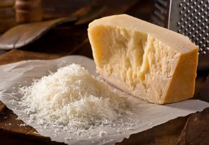 Un pezzo di Parmigiano Reggiano accanto a una montagnetta di formaggio grattugiato. Si può congelare il parmigiano grattugiato per averlo sempre pronto.