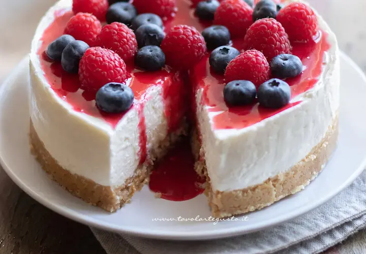 Delizioso cheesecake con mascarpone, guarnito con lamponi freschi, mirtilli e una colata di salsa rossa.