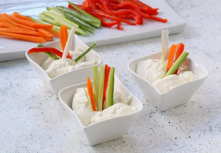 Tre ciotoline con mousse di caprino e bastoncini di verdure fresche: carote, cetrioli e peperoni rossi.
