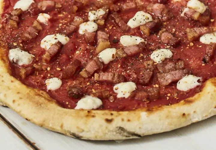 Pizza con guanciale croccante, pomodoro e fiocchi di pecorino, un sapore intenso e autentico.