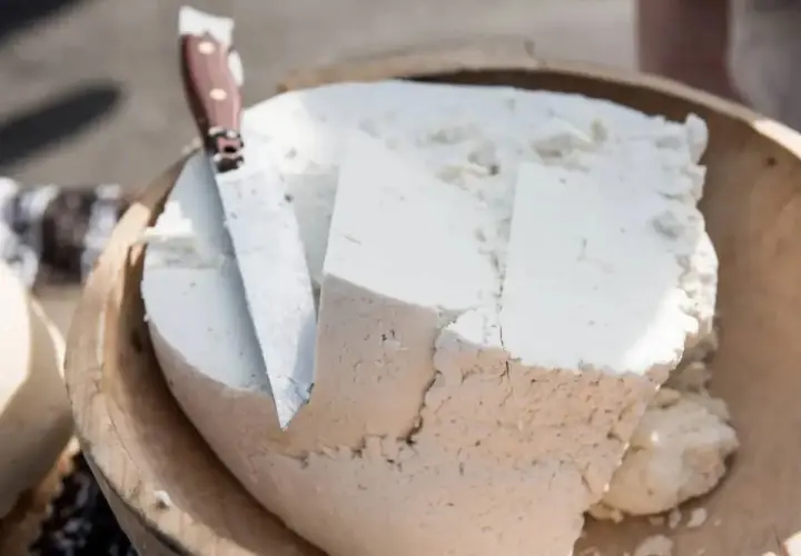 Formaggio fresco e morbido, simile a uno stracchino, tagliato in una ciotola di legno con un coltello.