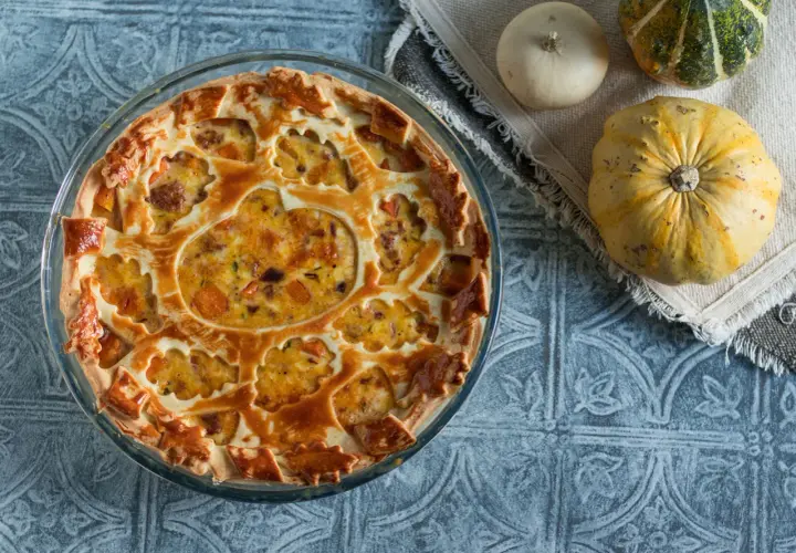 Torta salata zucca salsiccia e stracchino, con decorazione a intreccio e ripieno dorato. Accanto, zucche decorative.