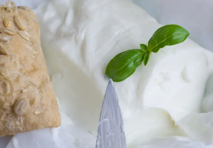 Un panino integrale con semi e un blocco di cremoso stracchino, un formaggio magro, guarnito con una foglia di basilico.