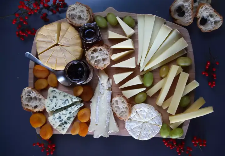Un tagliere ricco di formaggio di capra francese, accompagnato da pane croccante, uva, albicocche secche e marmellata.