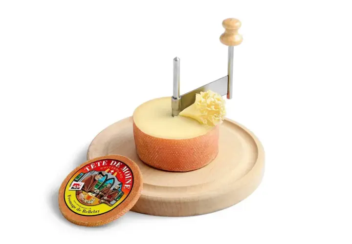 Forme di formaggio Tête de Moine su tagliere di legno, con girolle per creare riccioli.