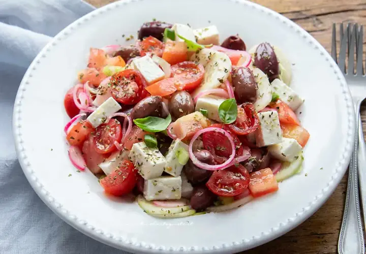 Insalata fresca con pomodorini, olive, cipolla rossa e cubetti di feta, condita con erbe aromatiche.