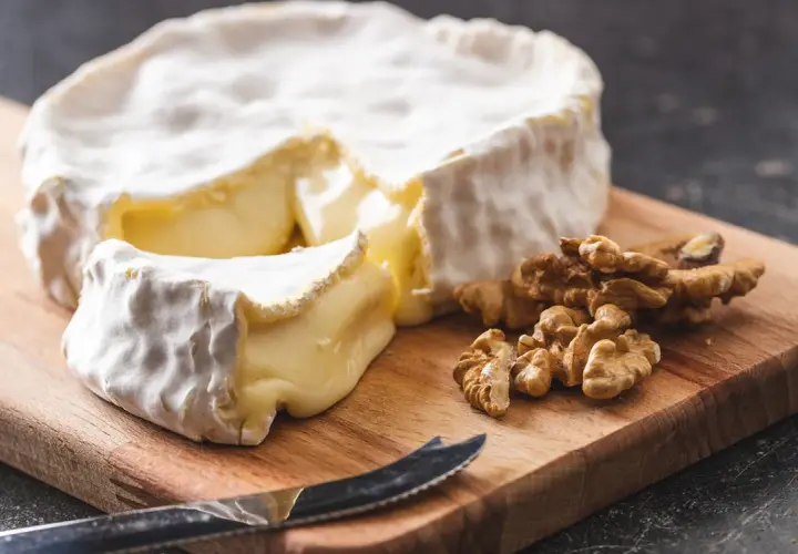 Un pezzo di brie, un formaggio grasso, su un tagliere con noci e un coltello.