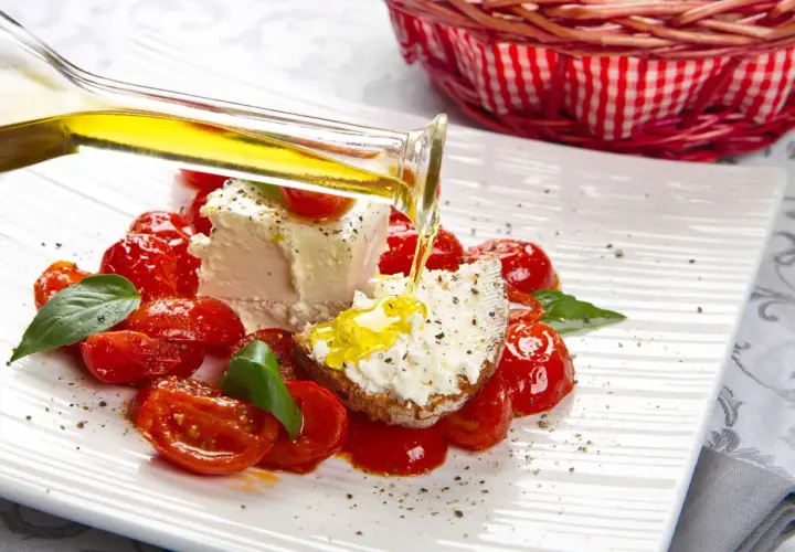 Un piatto di pomodorini confit con robiola, perfetto per un pasto leggero e nutriente in gravidanza. Olio d'oliva versato su una fetta di pane con formaggio.