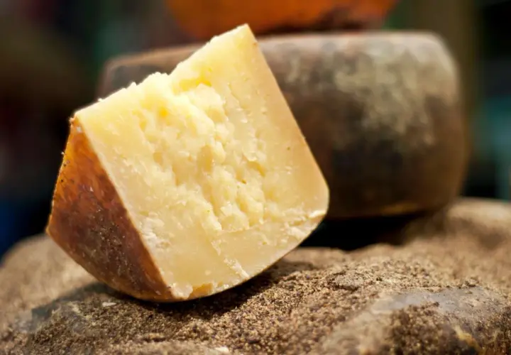 Un pezzo di formaggio sardo stagionato, con crosta scura e pasta gialla, riposa su un letto di spezie macinate.