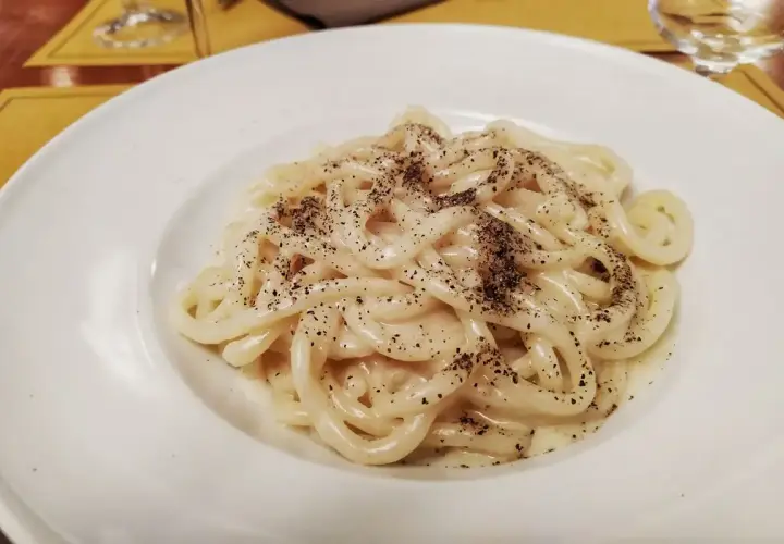 Pici cacio e pepe cremosi e fumanti, un classico della cucina romana, serviti su un piatto bianco.
