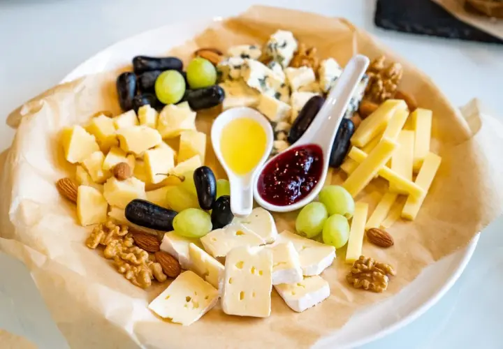Un tagliere ricco di formaggio semistagionato, uva, noci, mandorle, miele e marmellata.