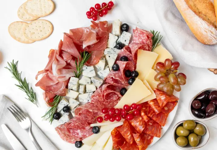 Un invitante piatto di formaggi con salumi, uva, olive e pane croccante, perfetto per un aperitivo.
