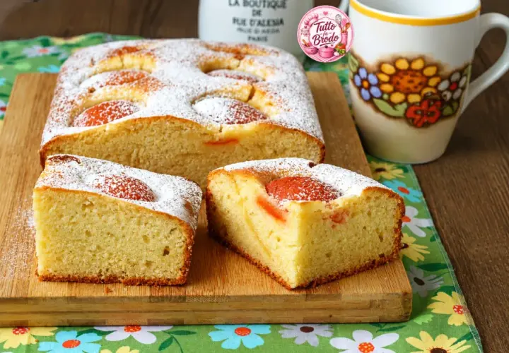 Torta albicocche e yogurt soffice, cosparsa di zucchero a velo, con pezzi di albicocca visibili. Perfetta per la colazione.