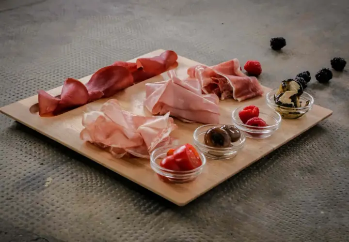 Un invitante tagliere di antipasti con salumi, olive, pomodorini e frutti di bosco, pronto per essere gustato.