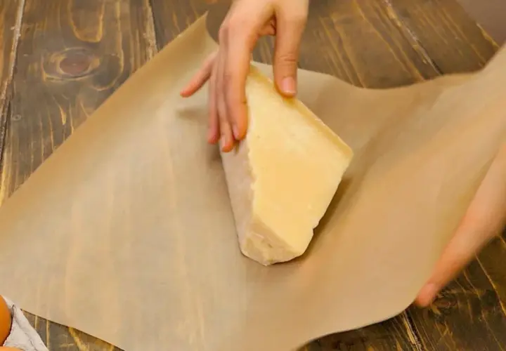 Mani che avvolgono un pezzo di formaggio stagionato nella carta forno, un metodo per conservare il formaggio al meglio.