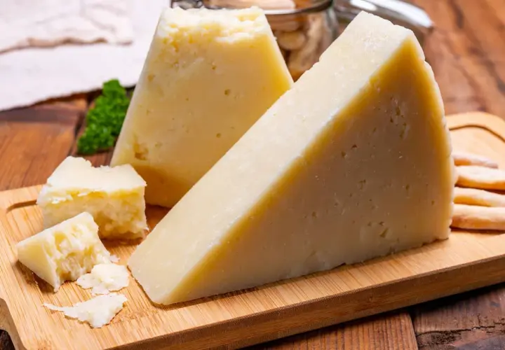 Fette di pecorino stagionato su tagliere di legno, con briciole e grissini sullo sfondo.
