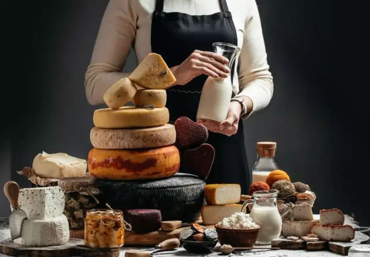 Una ricca selezione di formaggio a latte crudo, tra cui forme rotonde e quadrate, con latte fresco in caraffa.