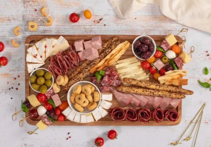 Un ricco antipasto salumi e formaggi su tagliere: salame, prosciutto, brie, taralli, olive e pomodorini.