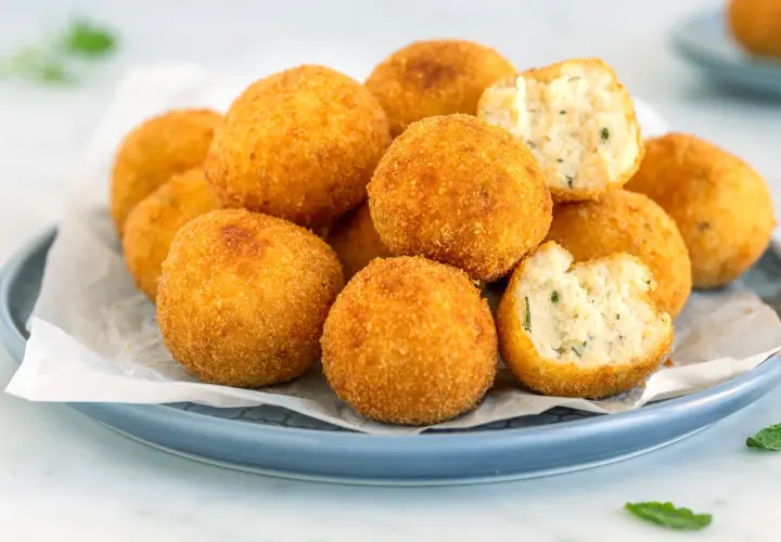 Arancini dorati e croccanti, perfetti per gustose ricette con ricotta. Uno è morso, rivelando un ripieno morbido e saporito.